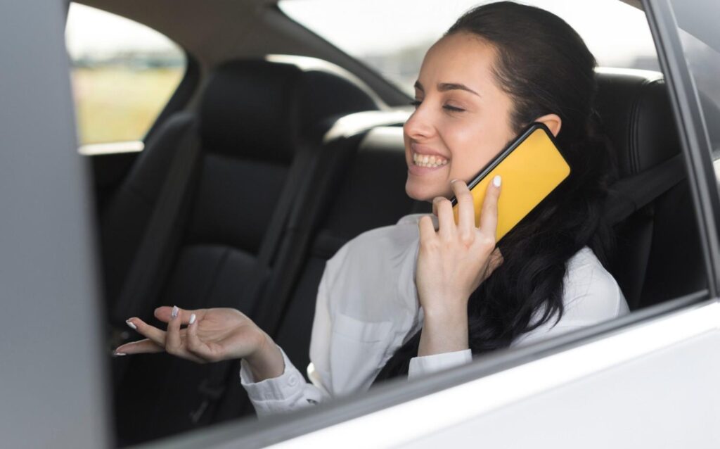 Smiling passenger talking on her smartphone while enjoying a premium airport taxi transit service.